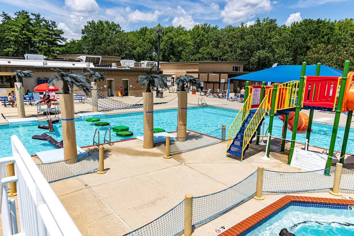 Outdoor splash area at Allentown Splash, Tennis, and Fitness Park with climbing play features and slides beside the main complex.
