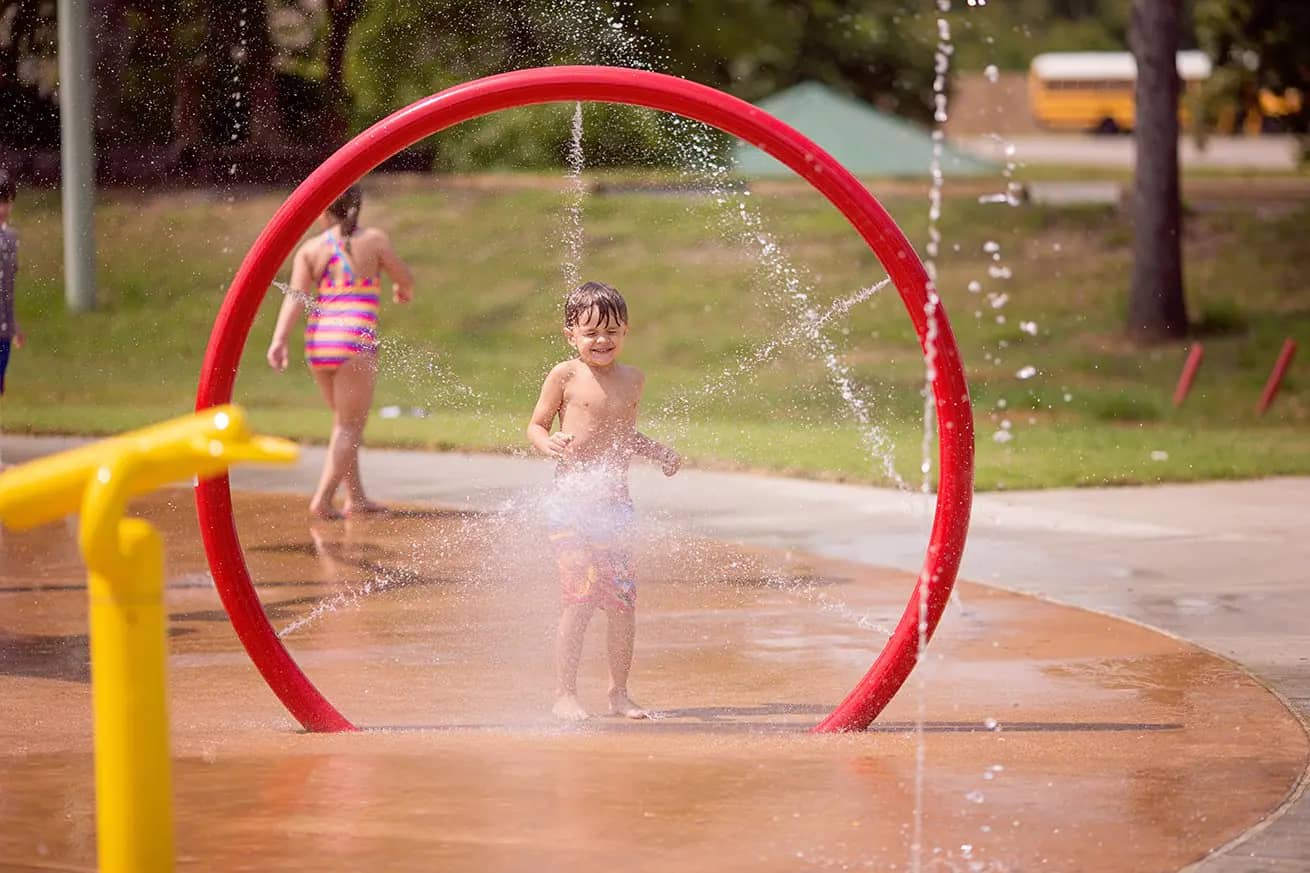 Official Tupelo splash pad photo with kids playing in open spray features.