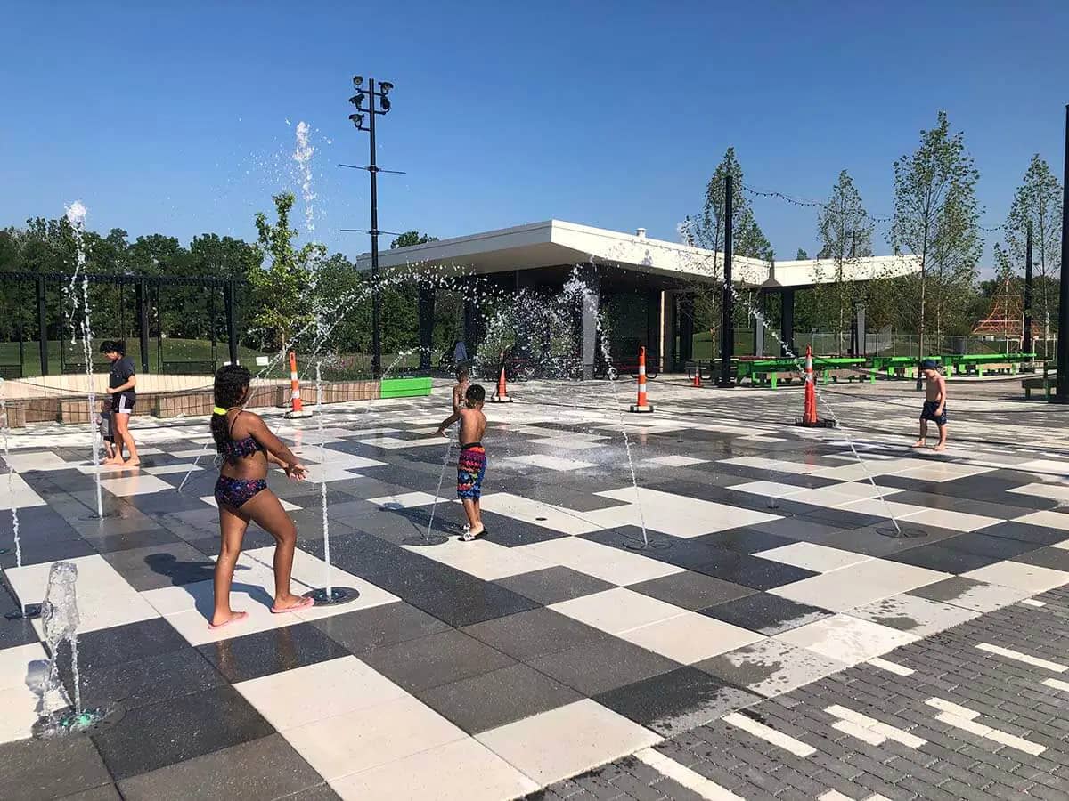 Kids playing among water jets at the Community Foundation Switchyard Plaza Spray Pad in Bloomington.