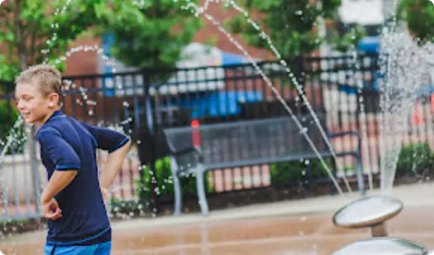 Zeeland Splash Pad Park with fenced splash area and shaded seating.