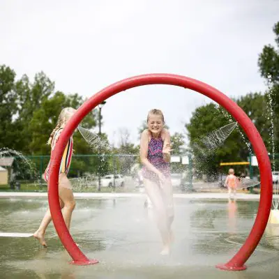 Children playing at a Minot splash pad with colorful spray features and seating nearby.